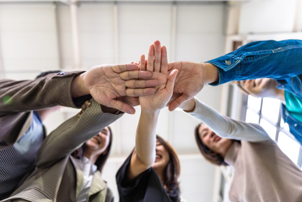 A diverse group of young professionals standing in a circle, putting their hands together in a team high-five