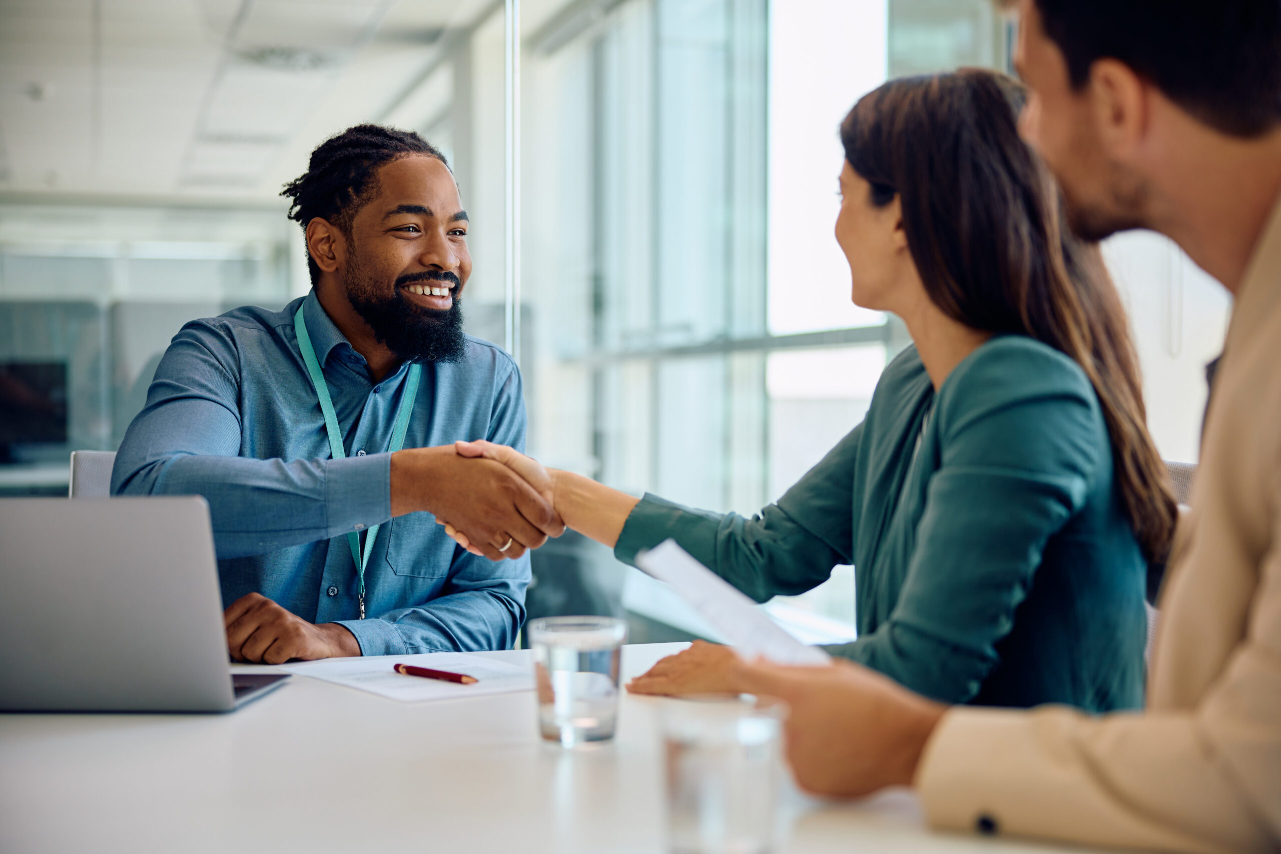 A young business professional happily shaking hands with a client in a modern office setting.